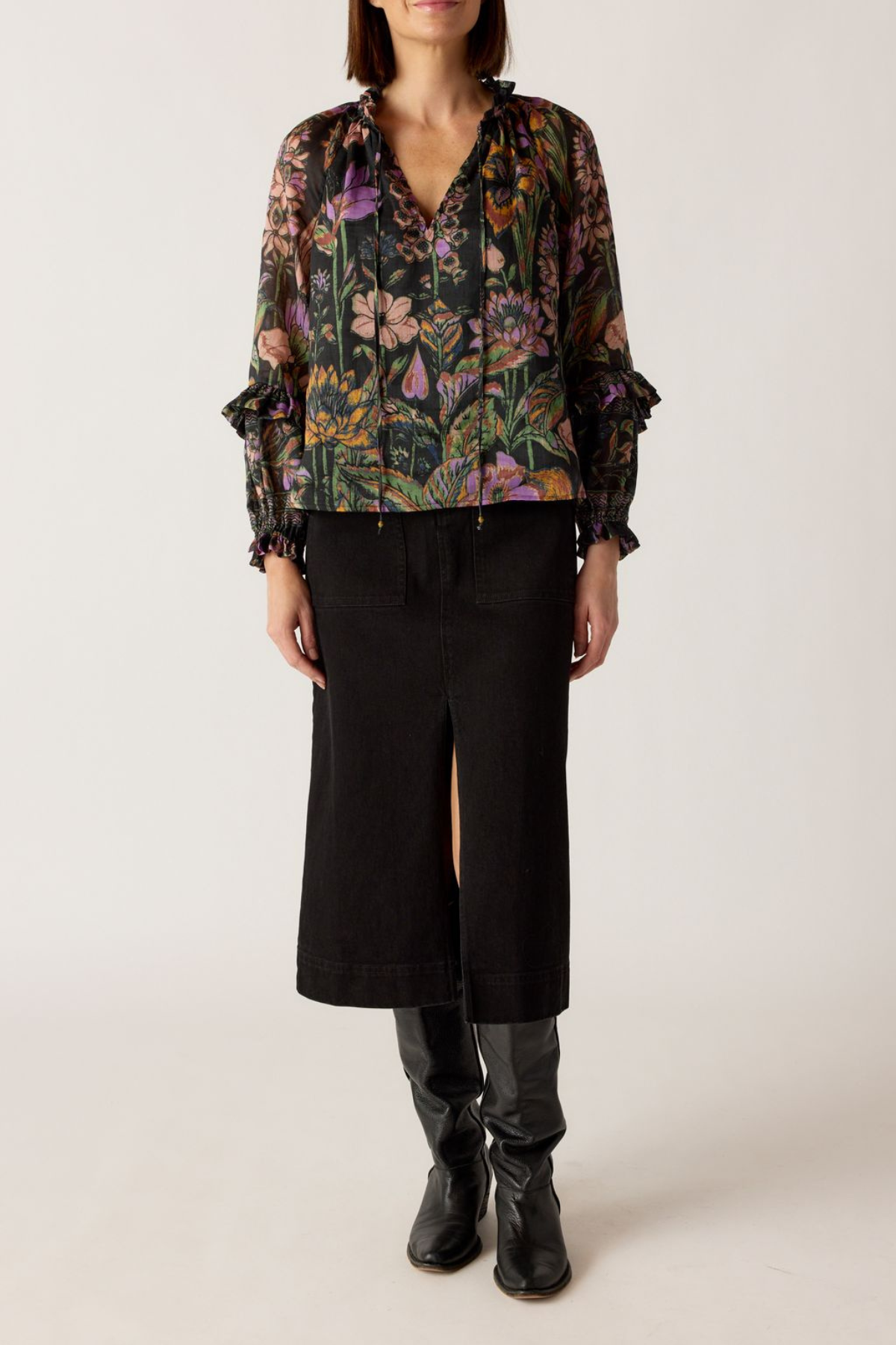 Person wearing a floral blouse and black skirt with black boots on a white background