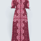 A long-sleeved maxi dress with puff sleeves and a front zipper, featuring a pink and deep magenta paisley and floral pattern, shown against a light gray background.