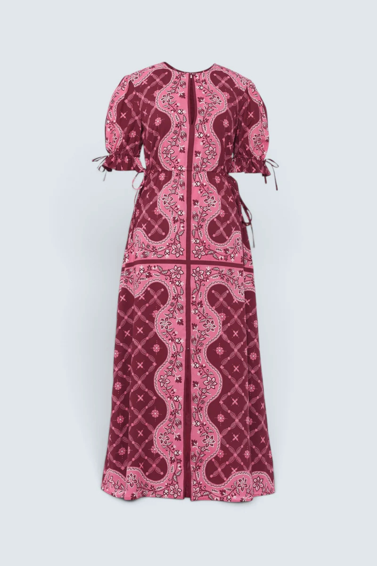A long-sleeved maxi dress with puff sleeves and a front zipper, featuring a pink and deep magenta paisley and floral pattern, shown against a light gray background.