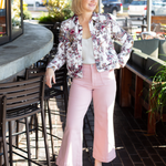 Woman in floral jacket and pink pants standing in an outdoor cafe setting