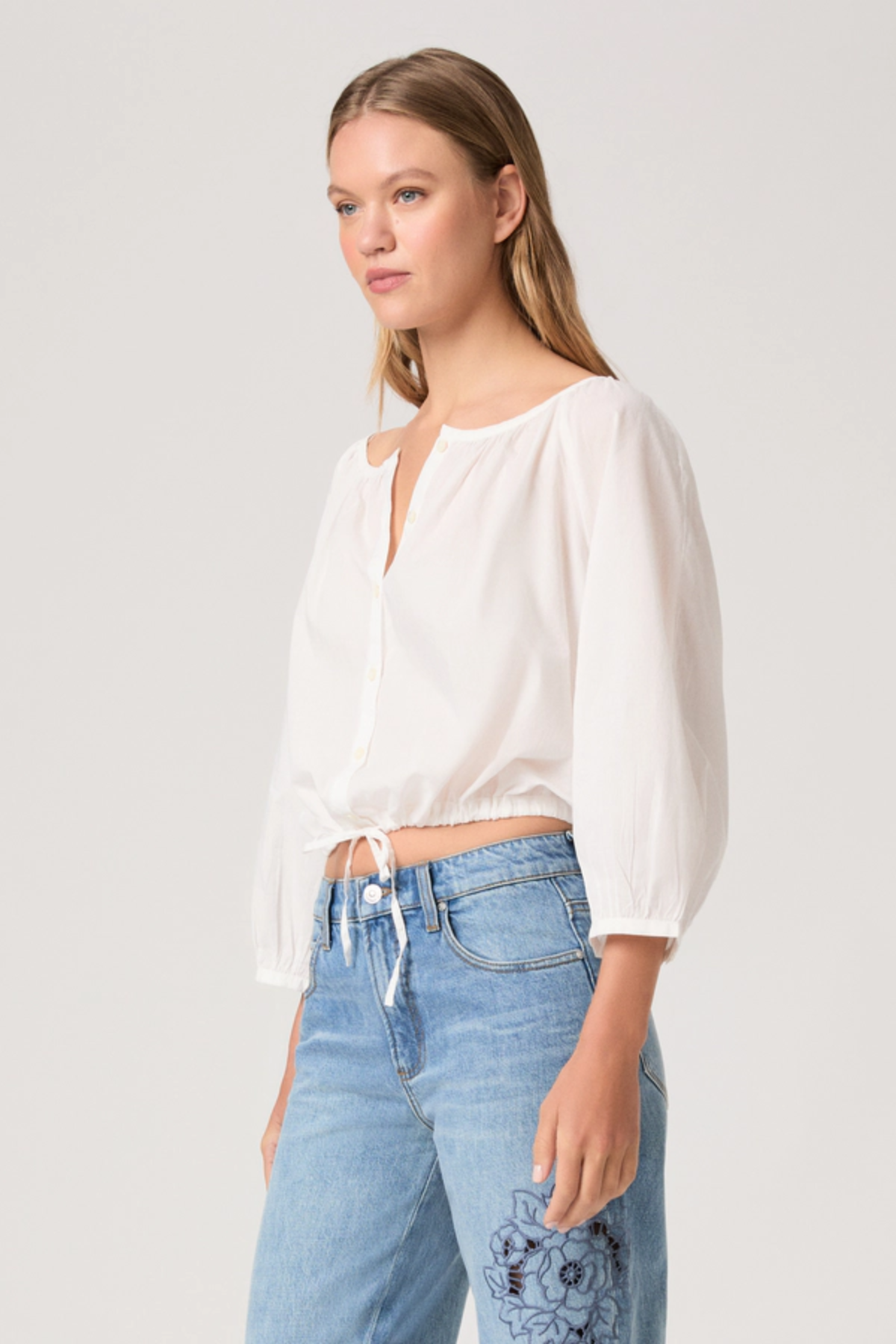 Woman wearing a white blouse and blue jeans on a plain background