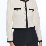 White jacket with black trim and gold buttons worn by a model on a white background