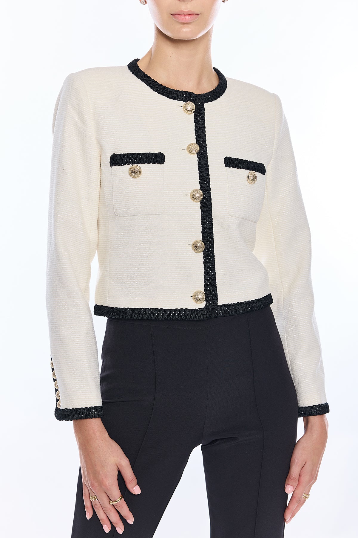 White jacket with black trim and gold buttons worn by a model on a white background