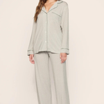 A woman modeling a light sage green waffle-knit pajama set with a long-sleeve button-front top and matching wide-leg pants, photographed against a plain beige studio background.