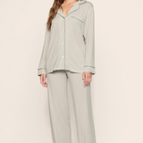 A woman modeling a light sage green waffle-knit pajama set with a long-sleeve button-front top and matching wide-leg pants, photographed against a plain beige studio background.