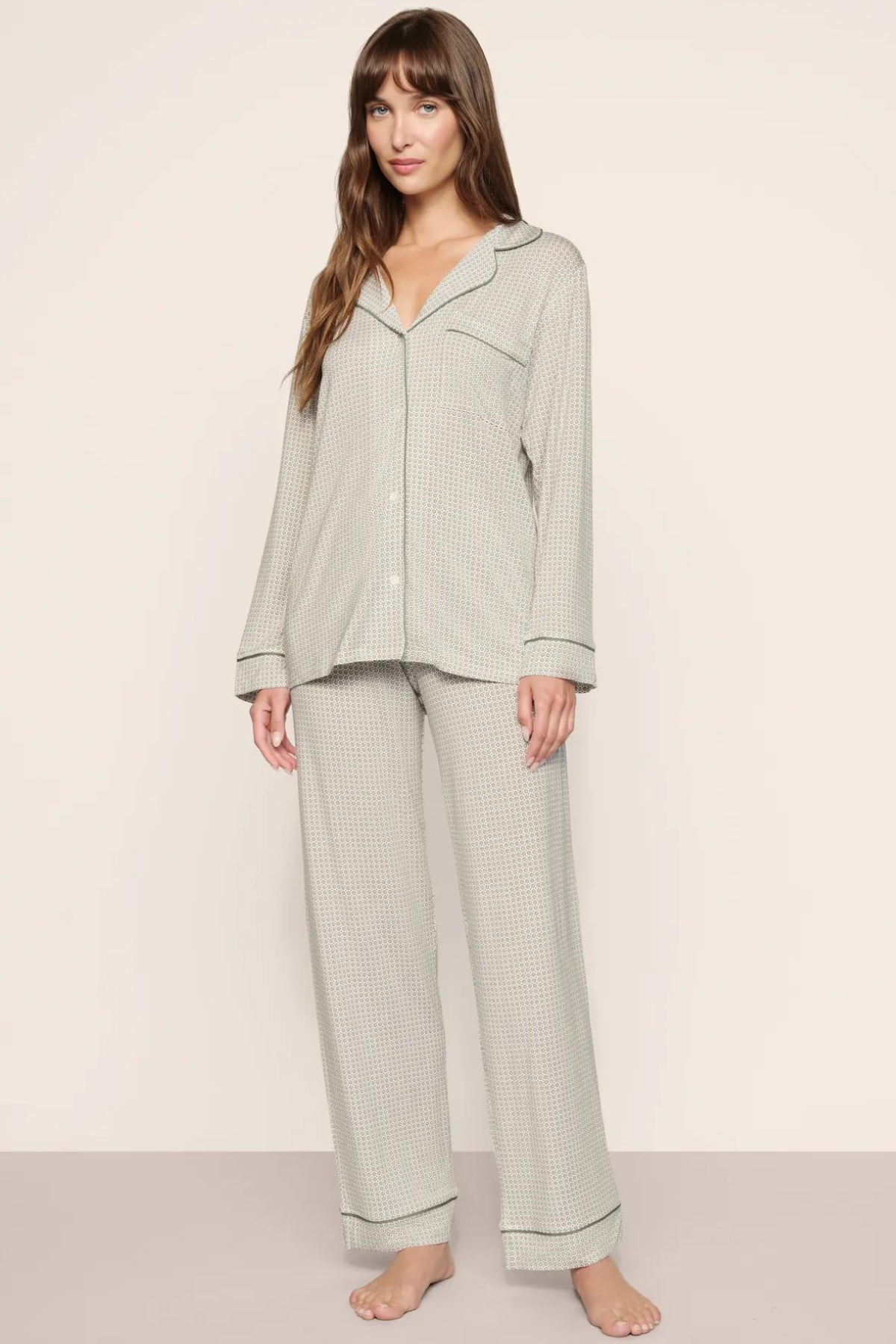 A woman modeling a light sage green waffle-knit pajama set with a long-sleeve button-front top and matching wide-leg pants, photographed against a plain beige studio background.