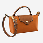 A structured leather handbag in warm camel brown with a darker brown flap, gold-tone hardware, a top handle, and a detachable shoulder strap, shown on a light gray background.
