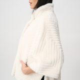 Woman wearing a white fur shrug against a plain background