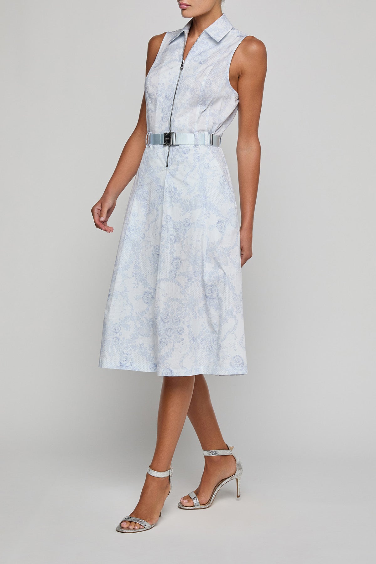 Woman wearing a light blue sleeveless dress with a belt on a gray background