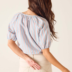 Woman wearing a striped blouse and beige pants against a plain background