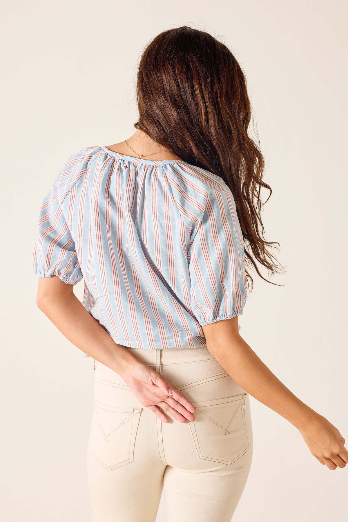 Woman wearing a striped blouse and beige pants against a plain background
