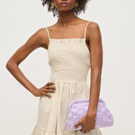 Woman wearing a beige dress holding a purple clutch against a white background