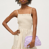 Woman wearing a beige dress holding a purple clutch against a white background