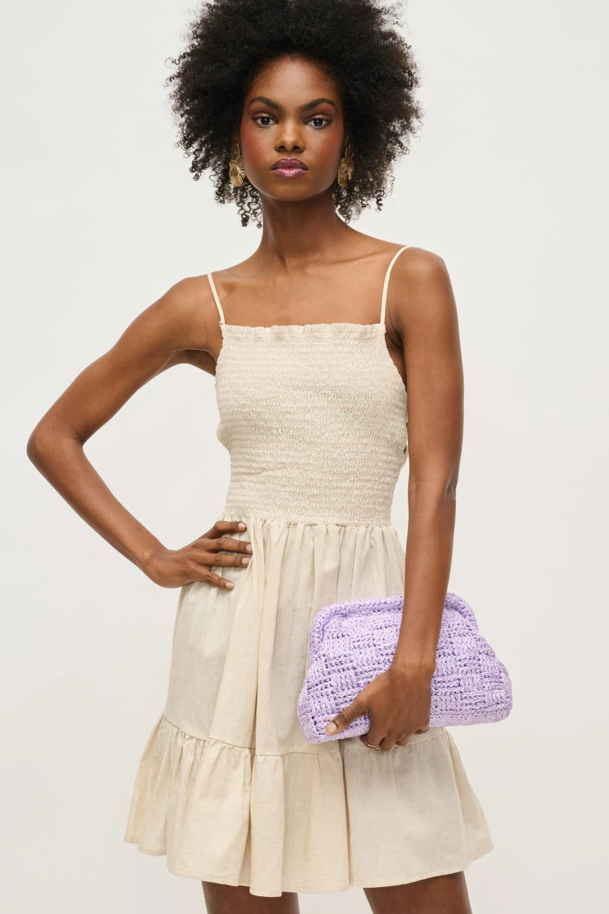 Woman wearing a beige dress holding a purple clutch against a white background