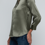 Model wearing dark green blouse with jeans on off white background.