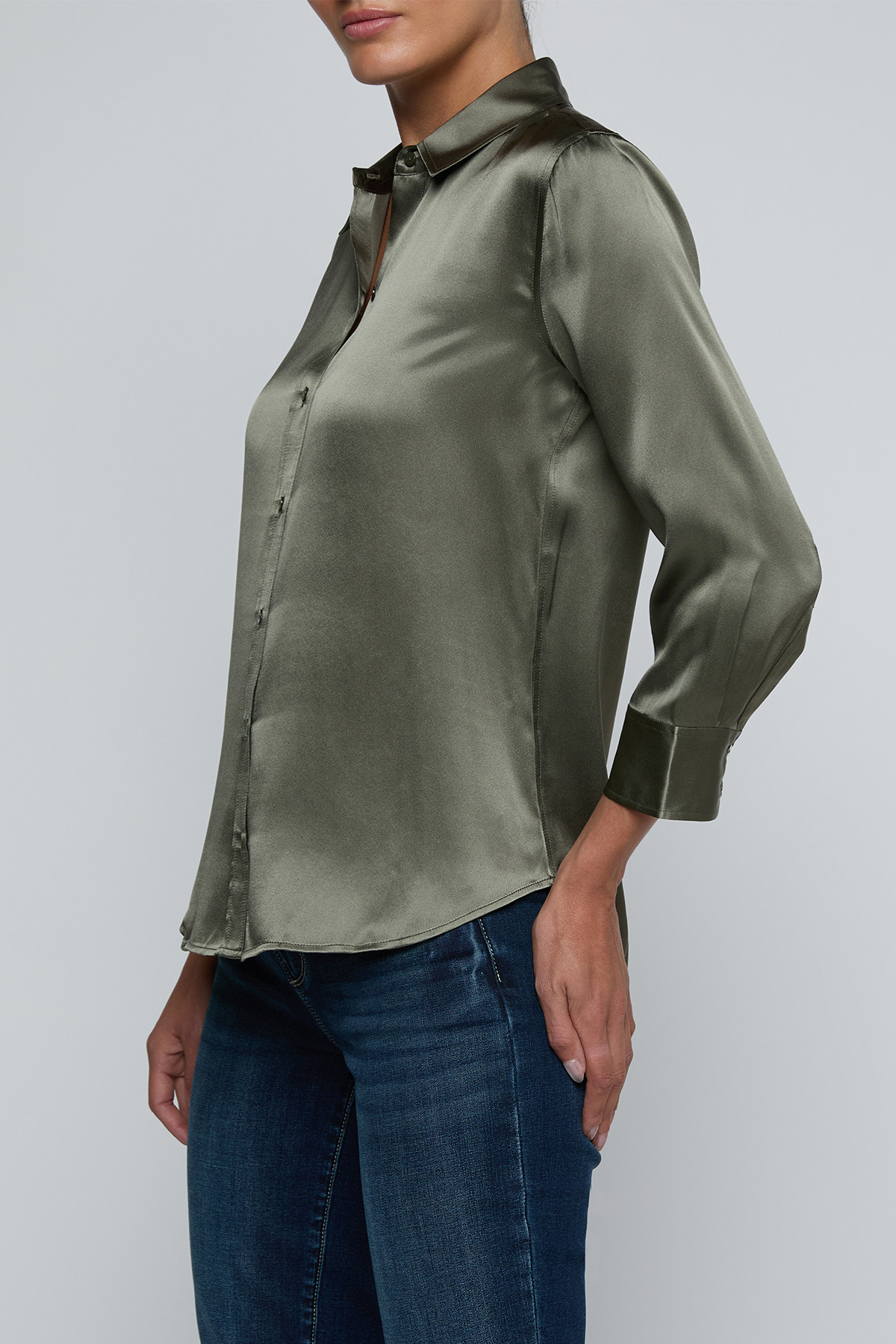 Model wearing dark green blouse with jeans on off white background.