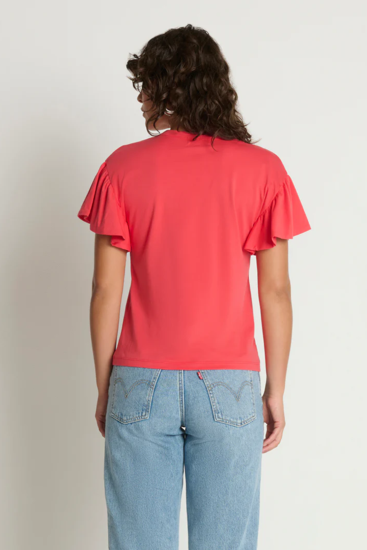 Person wearing a red t-shirt and blue jeans against a plain background