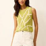 Woman wearing a green sleeveless knitted top with white patterns and white shorts on a beige background