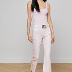 Woman wearing a light pink sleeveless top and pants with a belt, standing against a plain background.