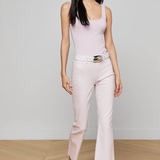 Woman wearing a light pink sleeveless top and pants with a belt, standing against a plain background.