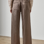 A person shown from the back wearing wide-leg taupe pants and a beige knit sweater, standing against a plain light gray wall and concrete floor.