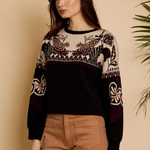 Woman wearing a black sweater with intricate patterns against a beige background
