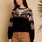 Woman wearing a black sweater with intricate patterns against a beige background