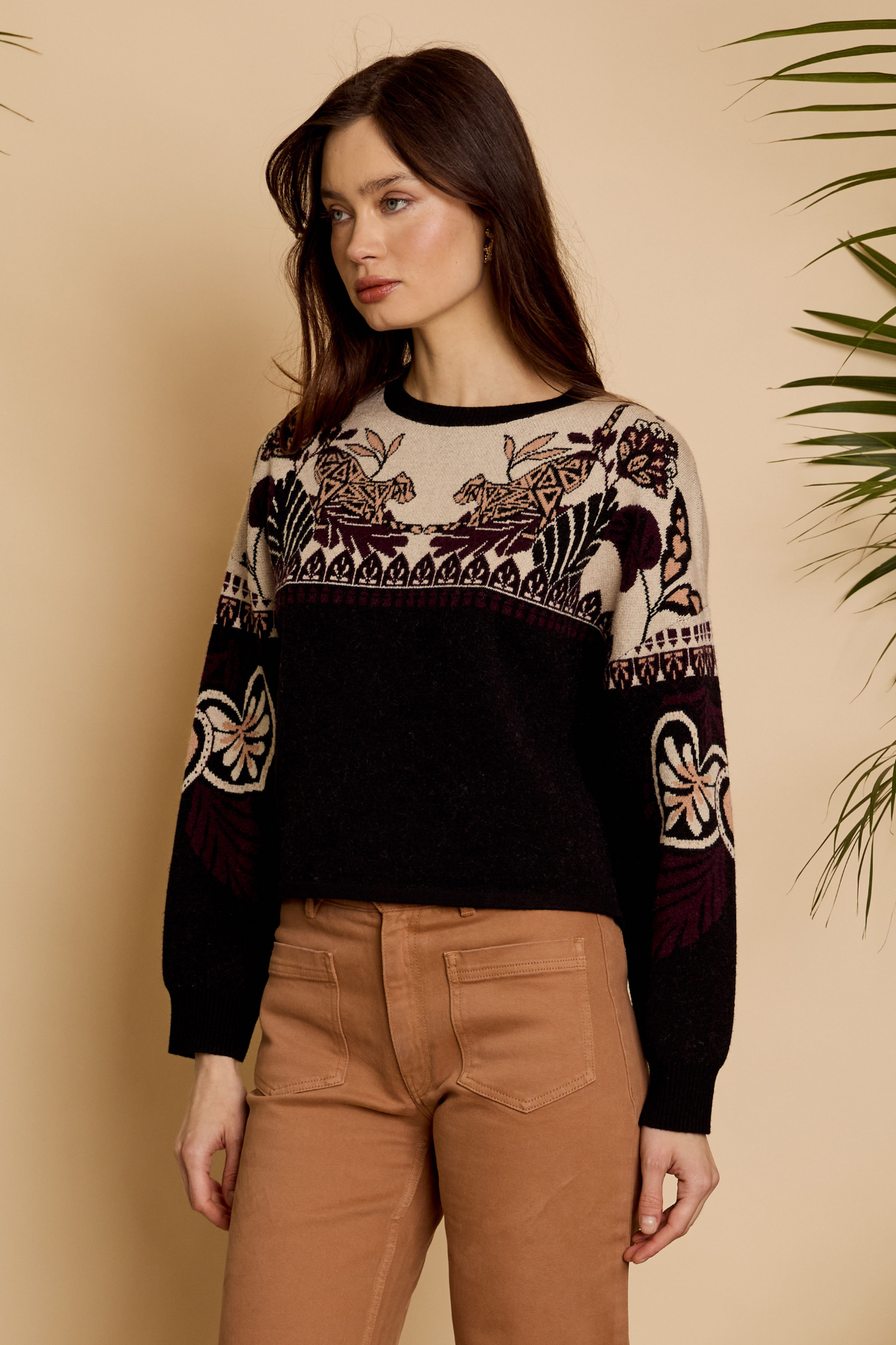 Woman wearing a black sweater with intricate patterns against a beige background