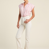 Woman wearing a pink striped shirt and white pants on a beige background