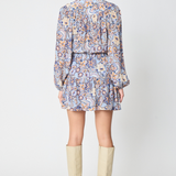 A woman shown from the back wearing a long-sleeve mini dress with a blue, orange, and beige paisley pattern, paired with beige knee-high boots, against a light gray studio background.