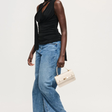 Woman wearing a black top and blue jeans, holding a beige handbag on a white background