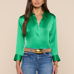 Woman wearing a green satin shirt and blue jeans against a beige background