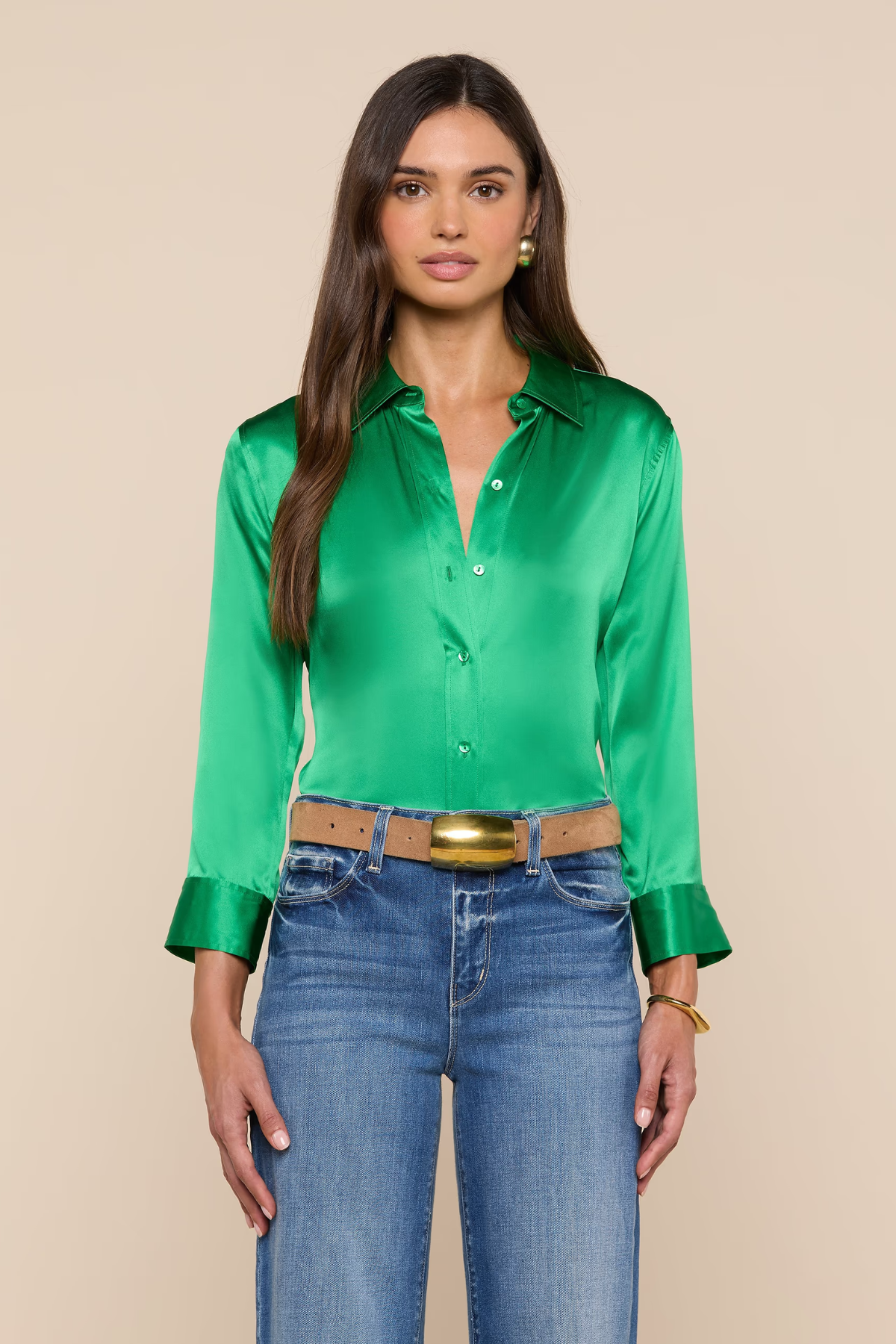 Woman wearing a green satin shirt and blue jeans against a beige background