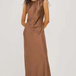 A woman modeling a sleeveless, midi-length brown satin dress with a high neckline and gathered shoulders, paired with black strappy high-heeled sandals against a plain white studio background.