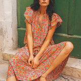 Woman in a floral dress sitting on stone steps with a green door in the background