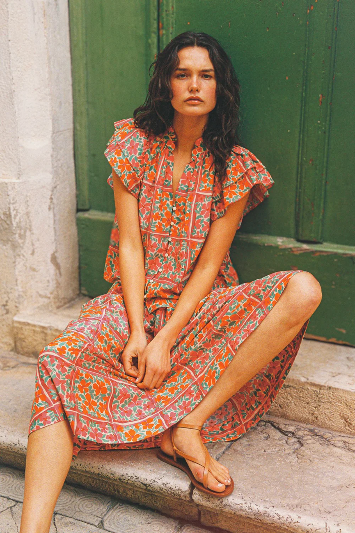 Woman in a floral dress sitting on stone steps with a green door in the background