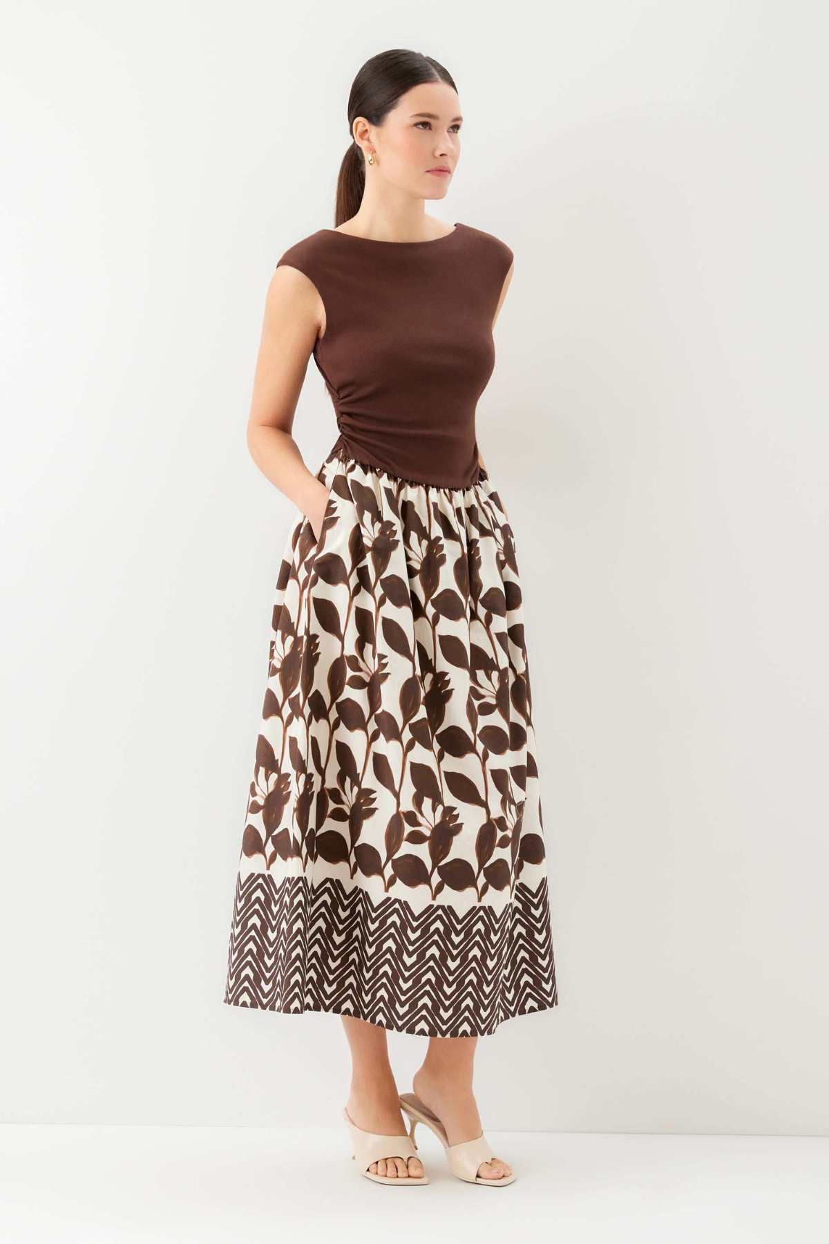 Woman wearing a brown top and patterned skirt on a white background