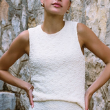 Woman wearing a textured white dress standing against a stone wall.