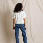 Person wearing a white t-shirt and blue jeans standing against a beige backdrop