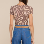 Model wearing swirl pattern tee with loose fitting jeans on beige background.