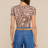 Model wearing swirl pattern tee with loose fitting jeans on beige background.
