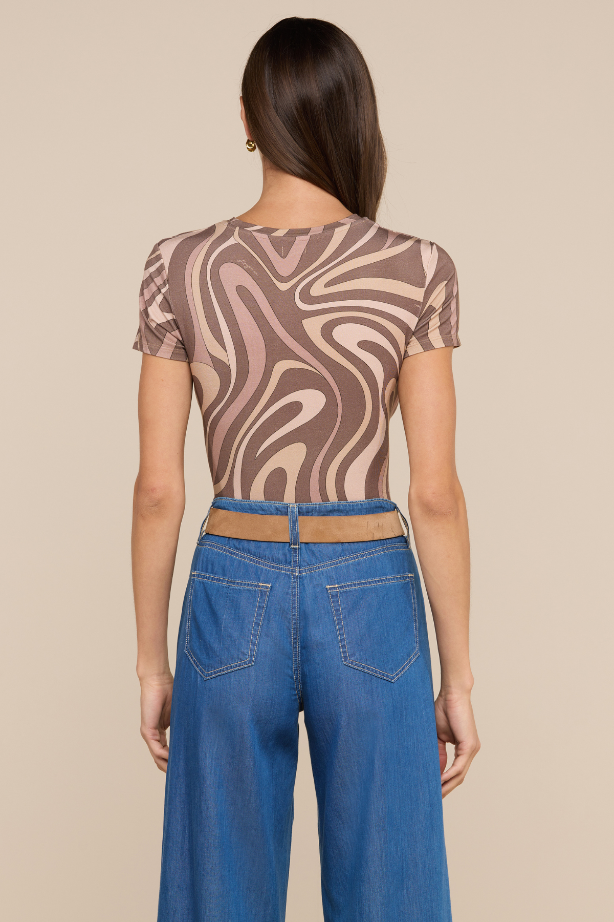 Model wearing swirl pattern tee with loose fitting jeans on beige background.