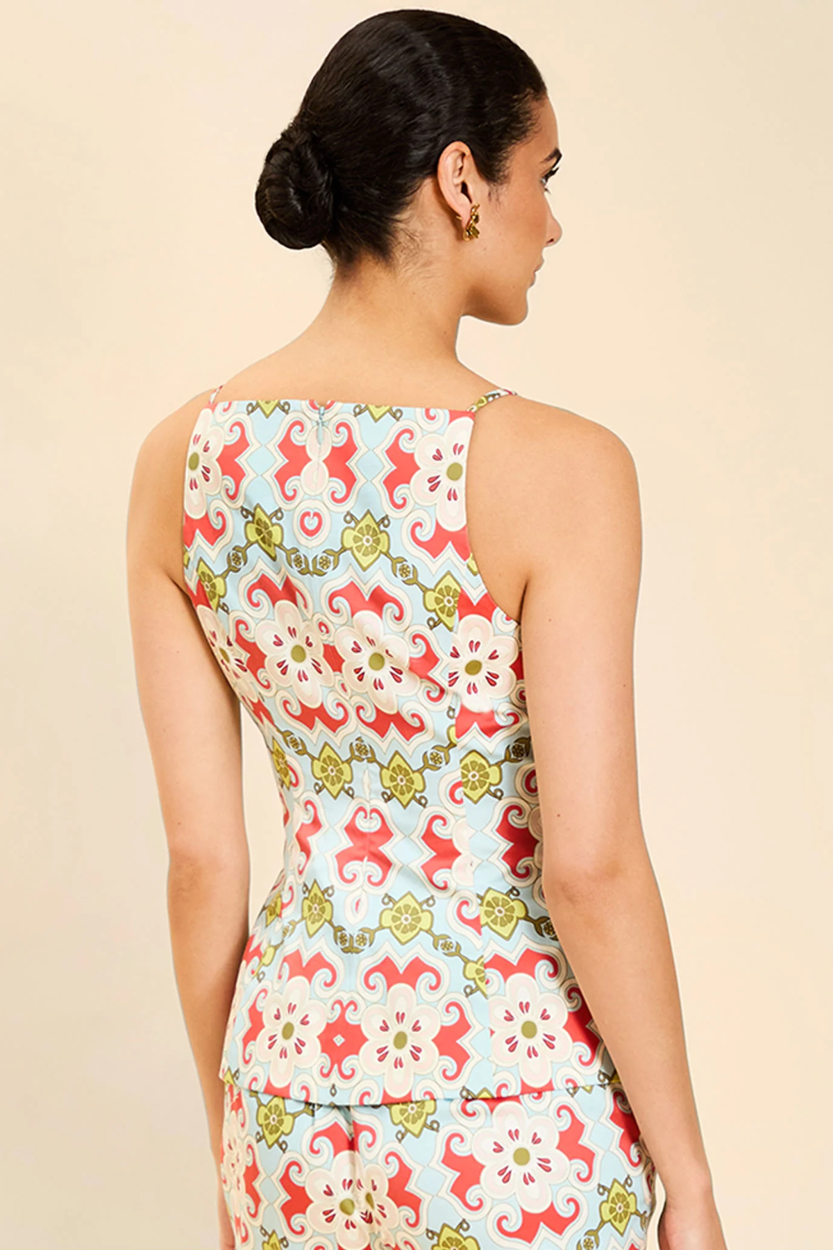 Woman wearing a sleeveless top with a colorful floral pattern on a beige background