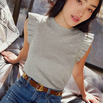 A woman sitting comfortably wearing a gray ruffled flutter sleeve tank top with a belt.