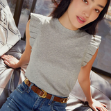 A woman sitting comfortably wearing a gray ruffled flutter sleeve tank top with a belt.
