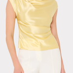 Woman wearing a yellow satin top and white pants on a light beige background