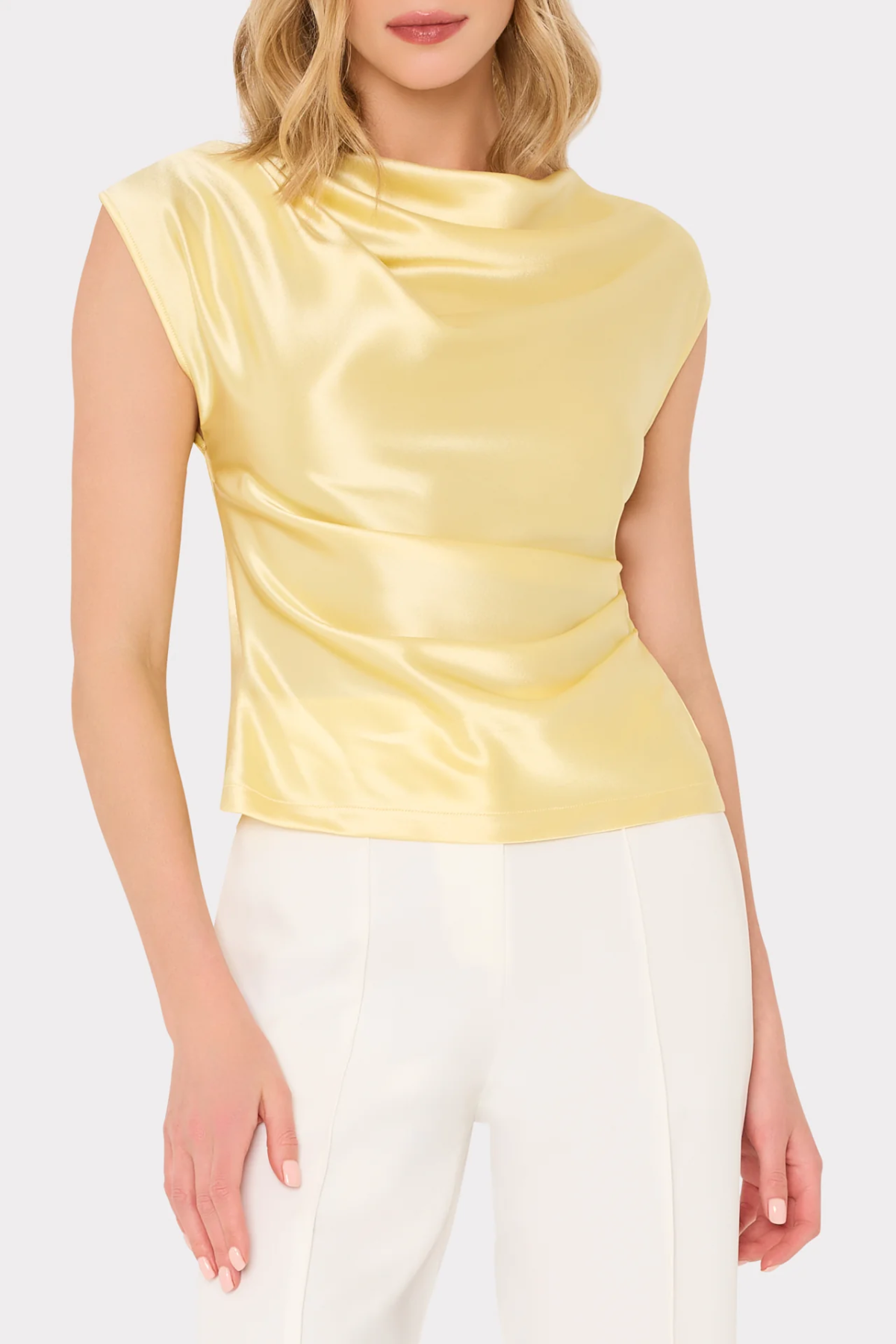 Woman wearing a yellow satin top and white pants on a light beige background