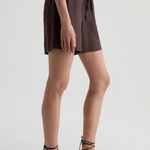 A model wearing dark brown linen shorts with a drawstring waist and black strappy flat sandals, shown from the waist down against a light gray studio background.