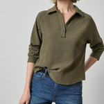 Woman wearing an olive green textured shirt and blue jeans on a gray background