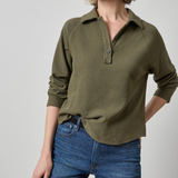 Woman wearing an olive green textured shirt and blue jeans on a gray background